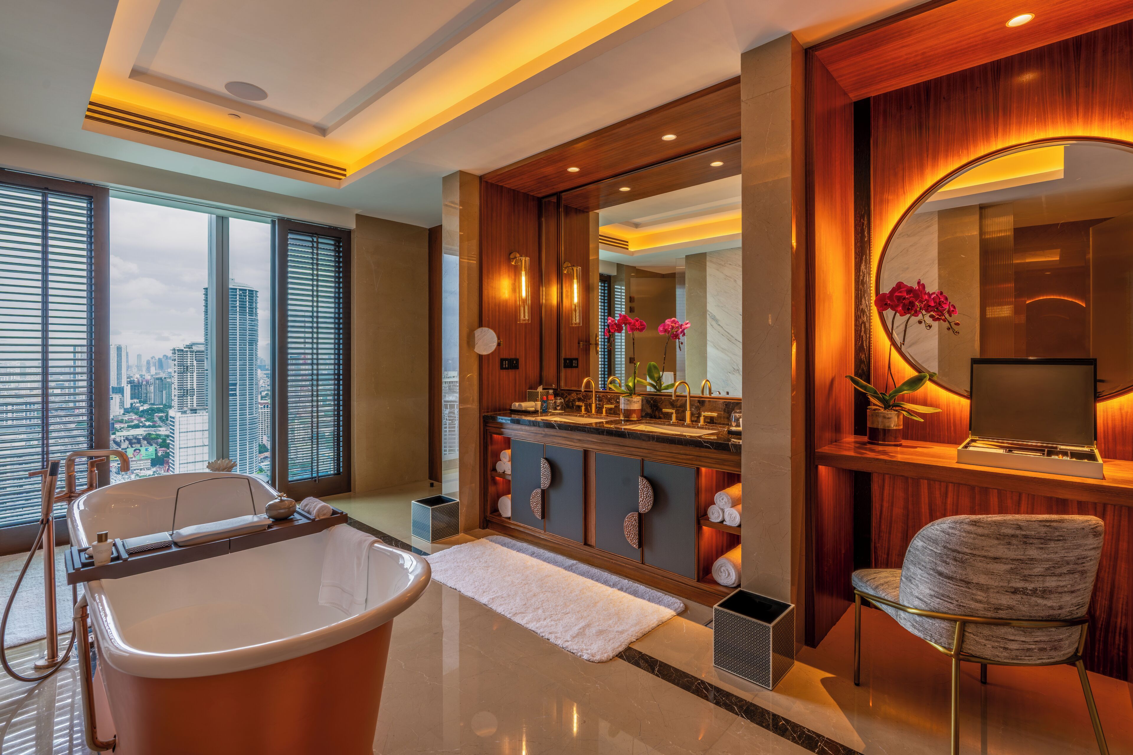 A modern bathroom with a bathtub, a vanity with a mirror, and a view of the city through large windows.
