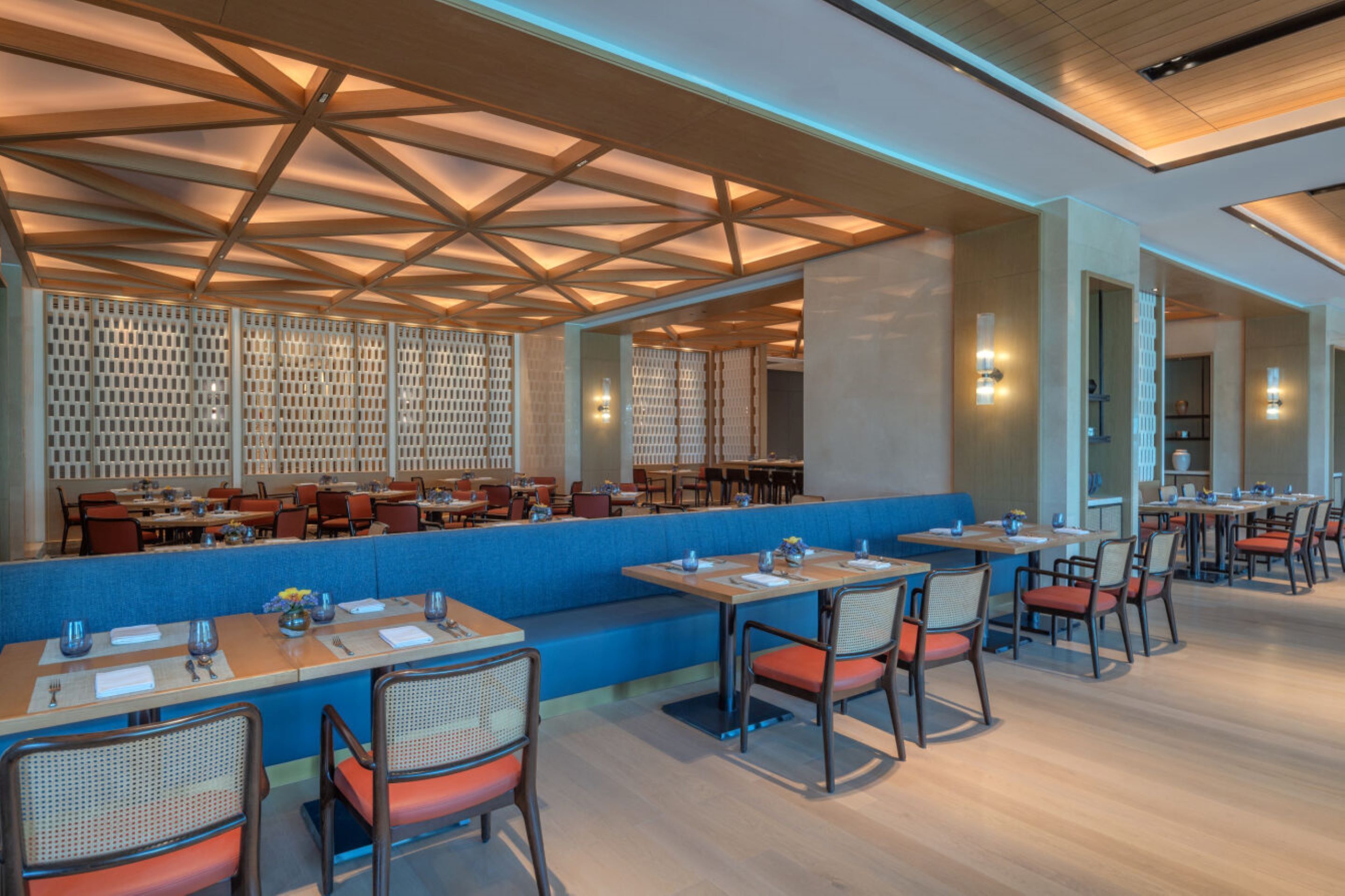 A modern restaurant with a geometric ceiling design, blue seating areas, and wooden tables.