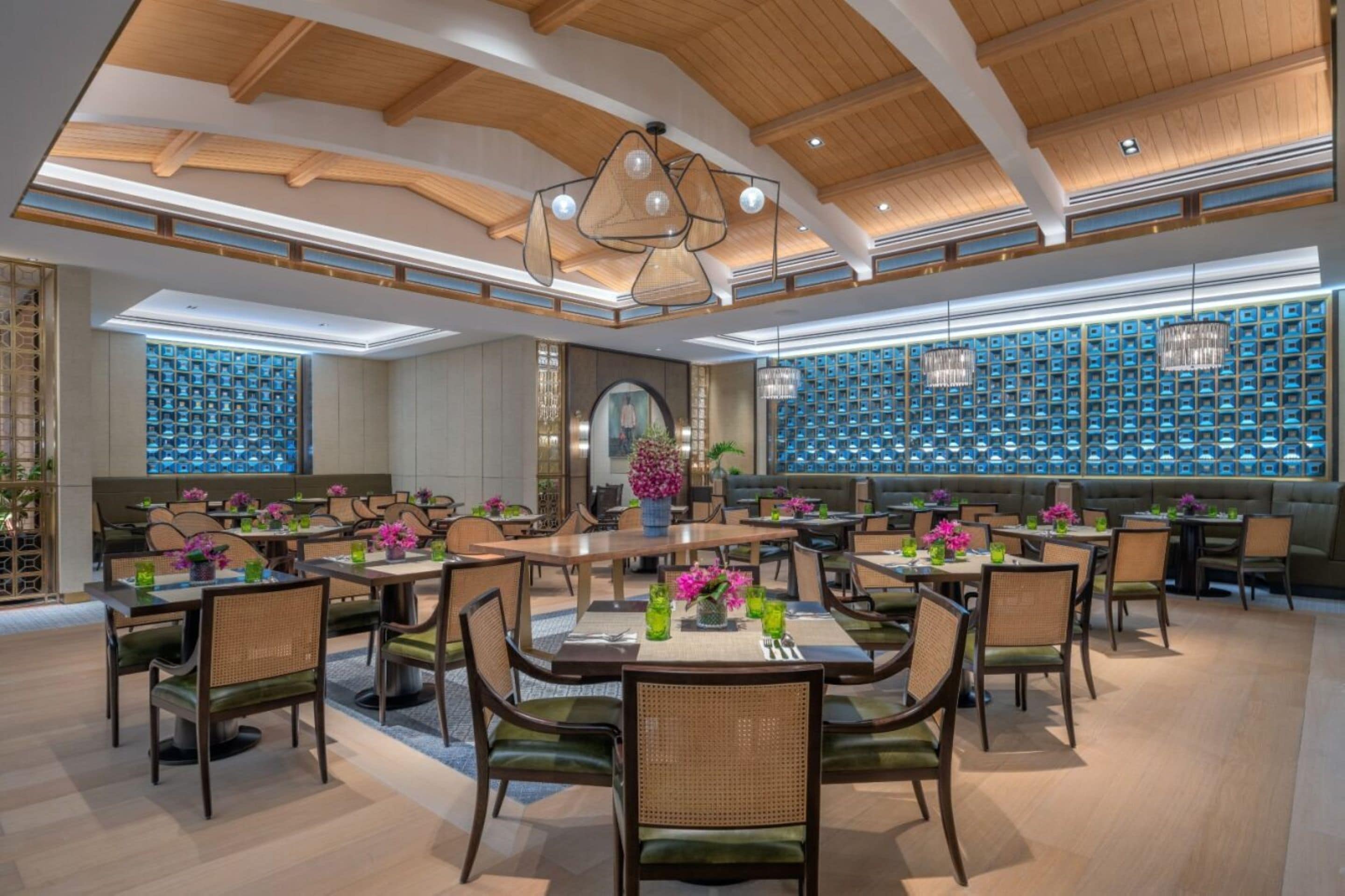 A spacious dining area with multiple tables and chairs, a wooden ceiling, and decorative lighting.