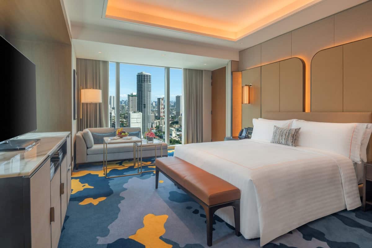 A modern hotel room with a large bed, a desk, a chair, and a view of the cityscape.