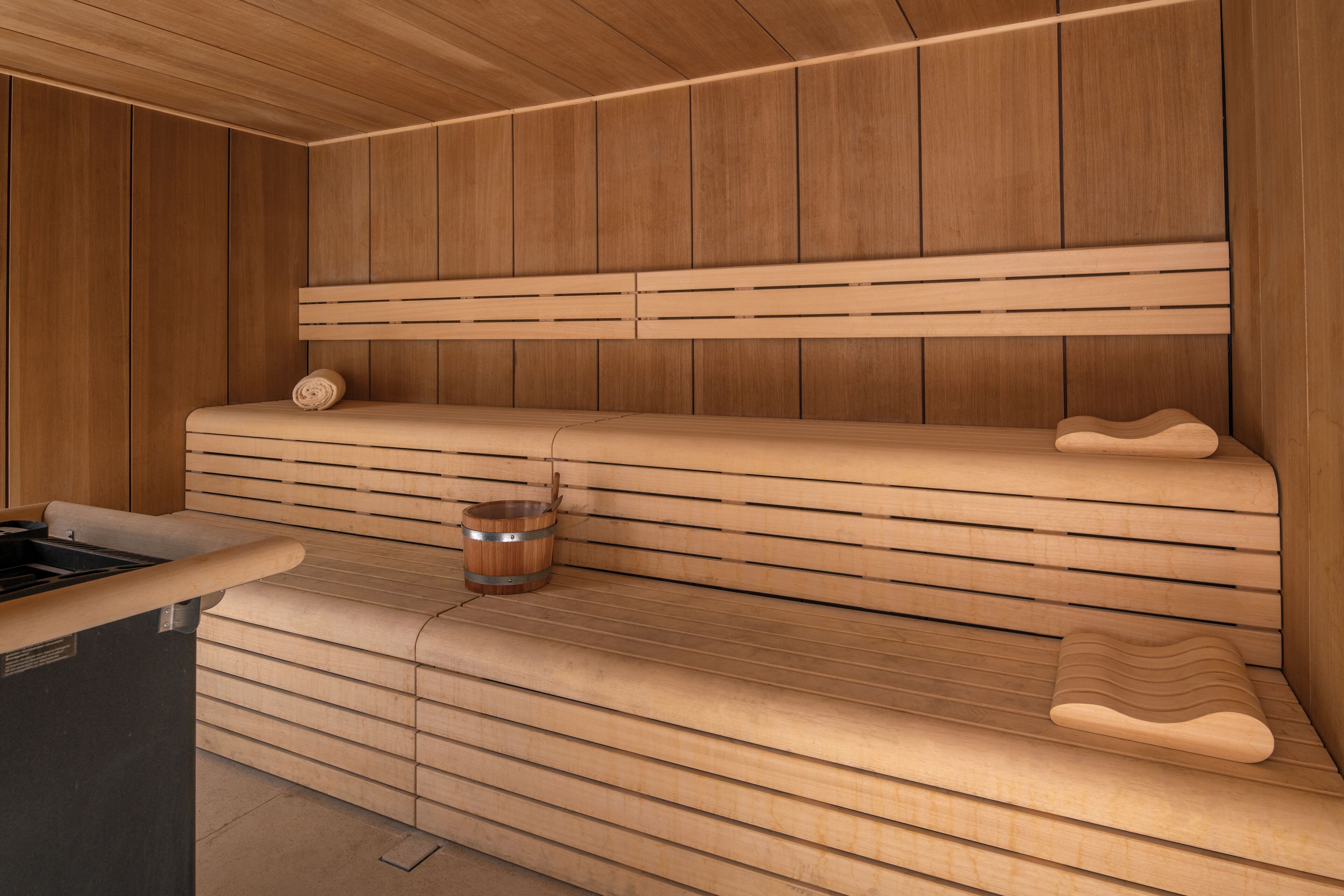 Una sauna con bancos de madera, una pared de madera y un cubo de metal.
