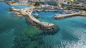 An aerial view of a coastal area with a marina, buildings, and a rocky breakwater.