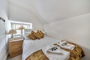 A bedroom with a bed, pillows, a bedside table, a lamp, and a window.