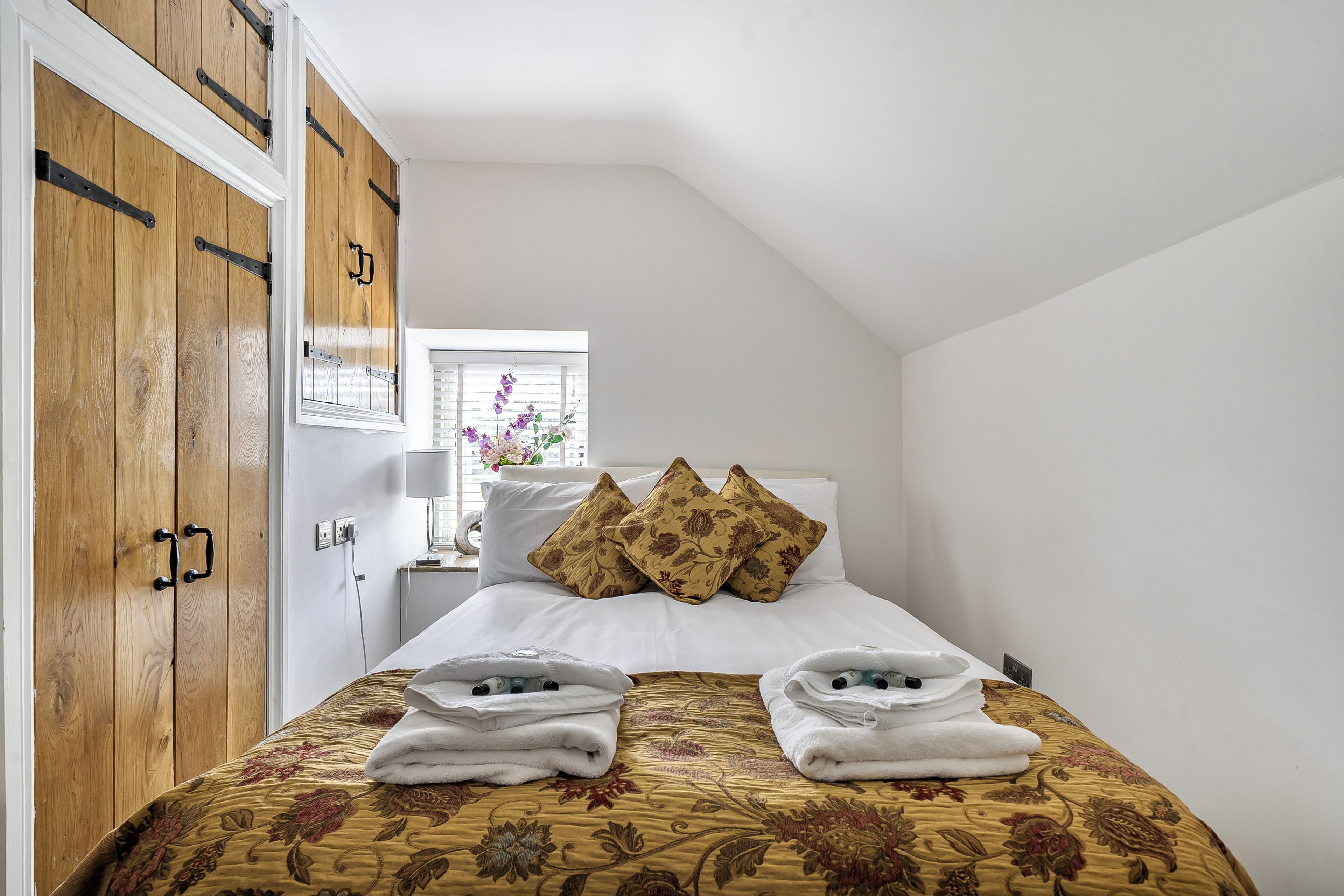 A hotel room with a bed, a wooden wardrobe, a nightstand, and a window with a view of the outside.