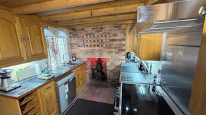 A compact kitchen with wooden cabinets, a brick wall, a built-in stove, and stainless steel appliances.