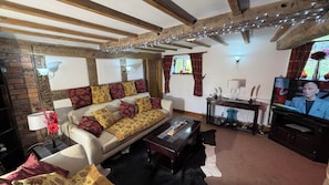 A cozy living room with exposed wooden beams, a sofa with patterned cushions, a coffee table, and a television.