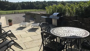 Une terrasse extérieure avec une table ronde, quatre chaises, un barbecue et une vue sur un champ verdoyant.