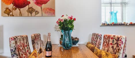 A dining table with a bottle of champagne, glasses, and a vase of flowers.