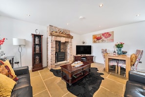 A living room with a fireplace, a television, a sofa, and a dining area with chairs.