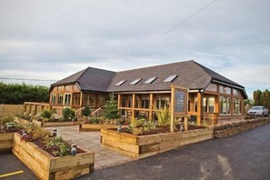 A building with a sloped roof, large windows, and wooden deck areas with planters. - Cosy Peak District Barn Conversion nr Alton Towers (WINKHILL NR LEEK)