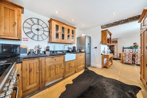 A kitchen with wooden cabinets, a large wall clock, a refrigerator, and a black rug.