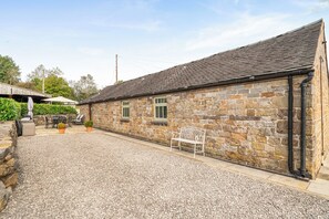 A stone building with a gravel courtyard, a metal bench, and outdoor furniture.