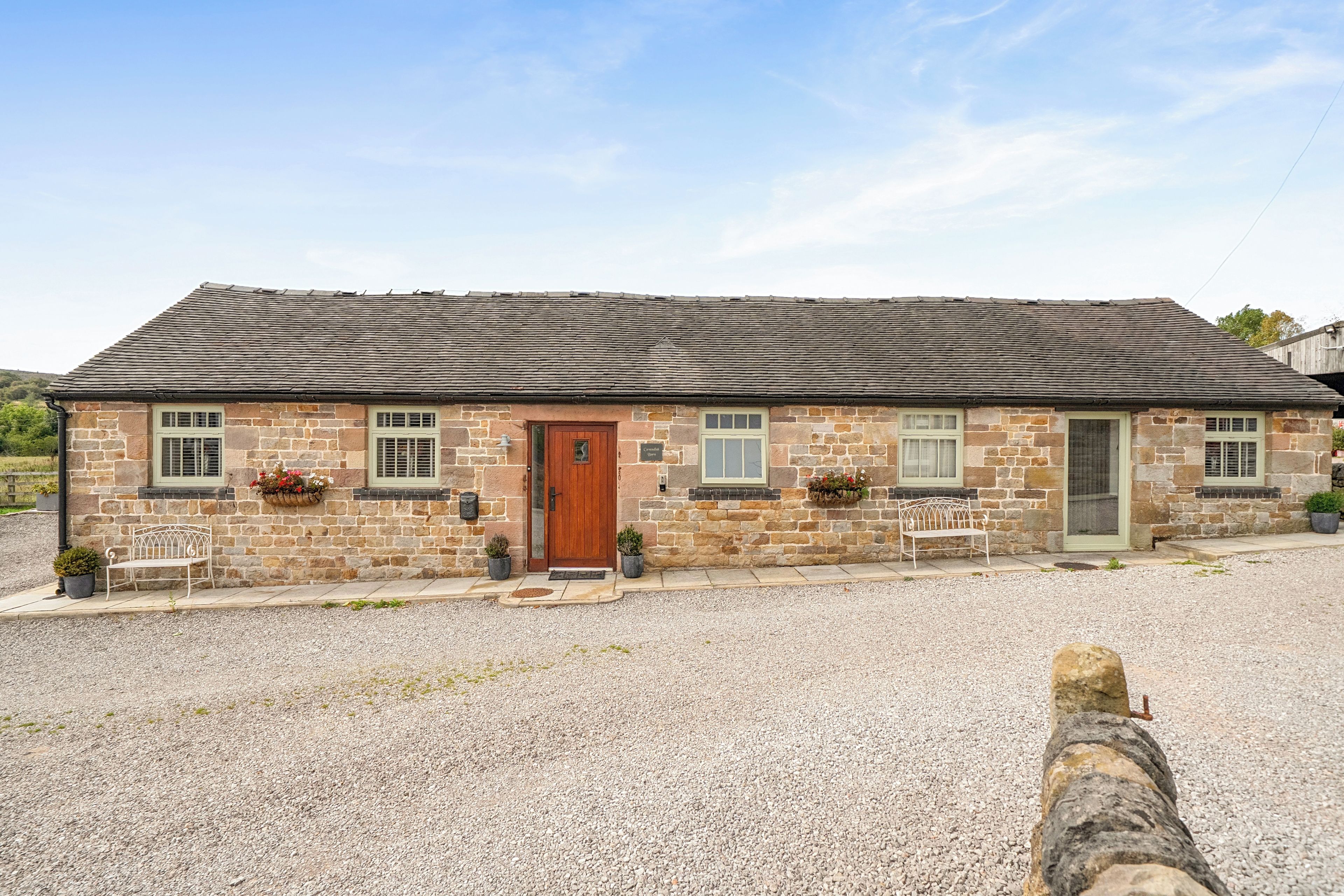 A stone building with a wooden door, windows, and a gravel driveway.