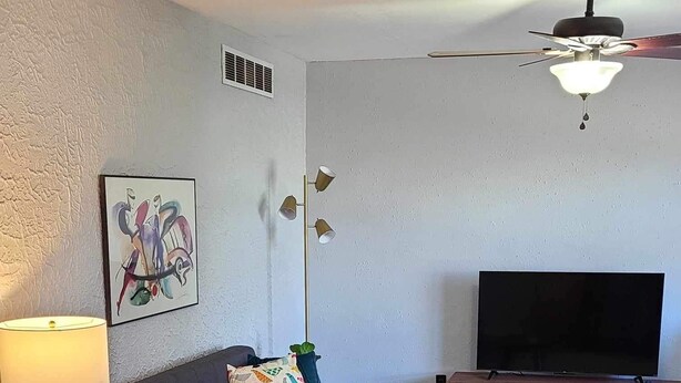 A living room with a sofa, coffee table, TV, and a ceiling fan.