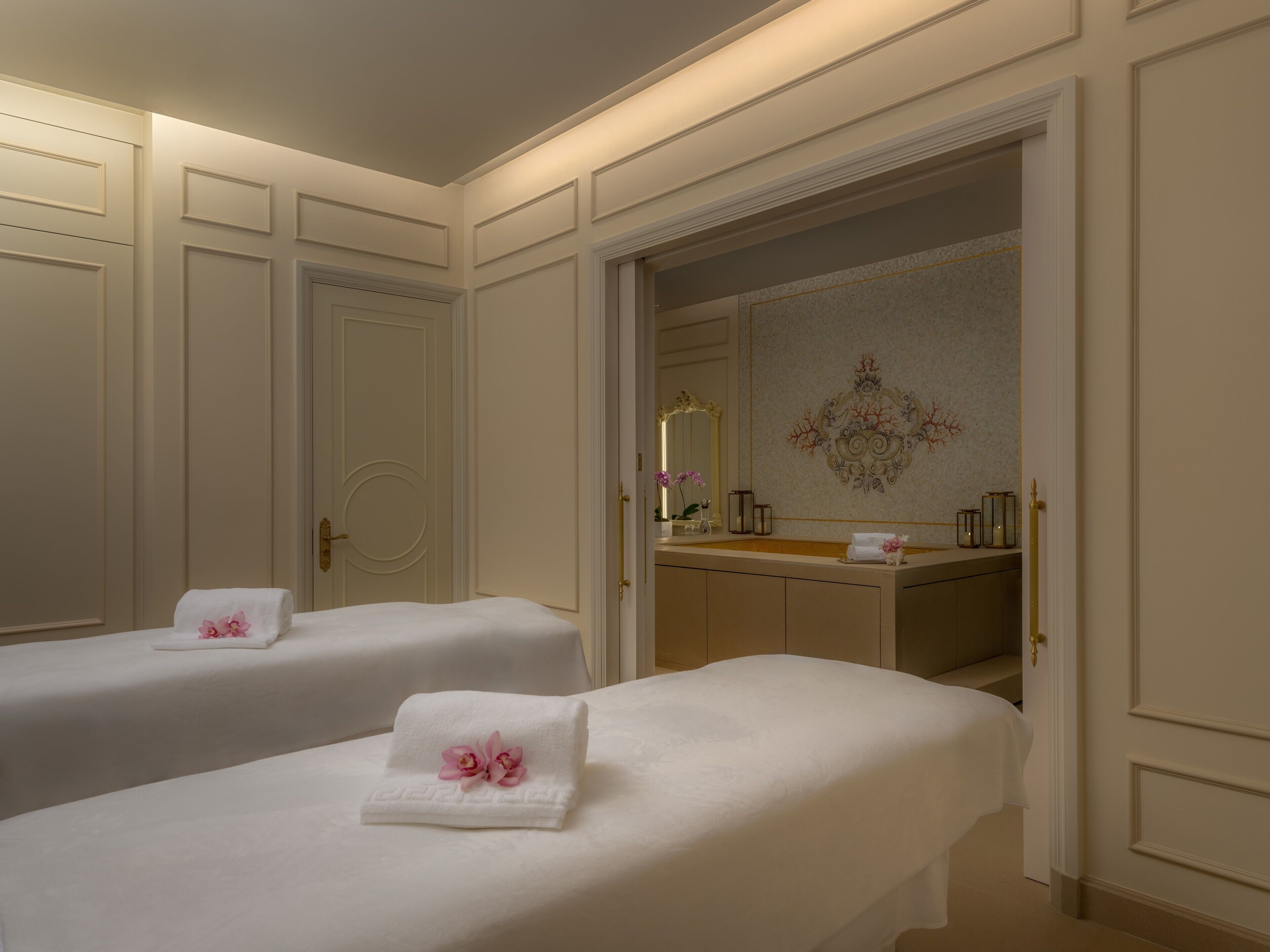 A hotel room with two beds, a bathroom with a mirror and sink, and a decorative wall.