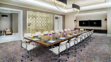 A conference room with a long table, white chairs, and a patterned carpet.
