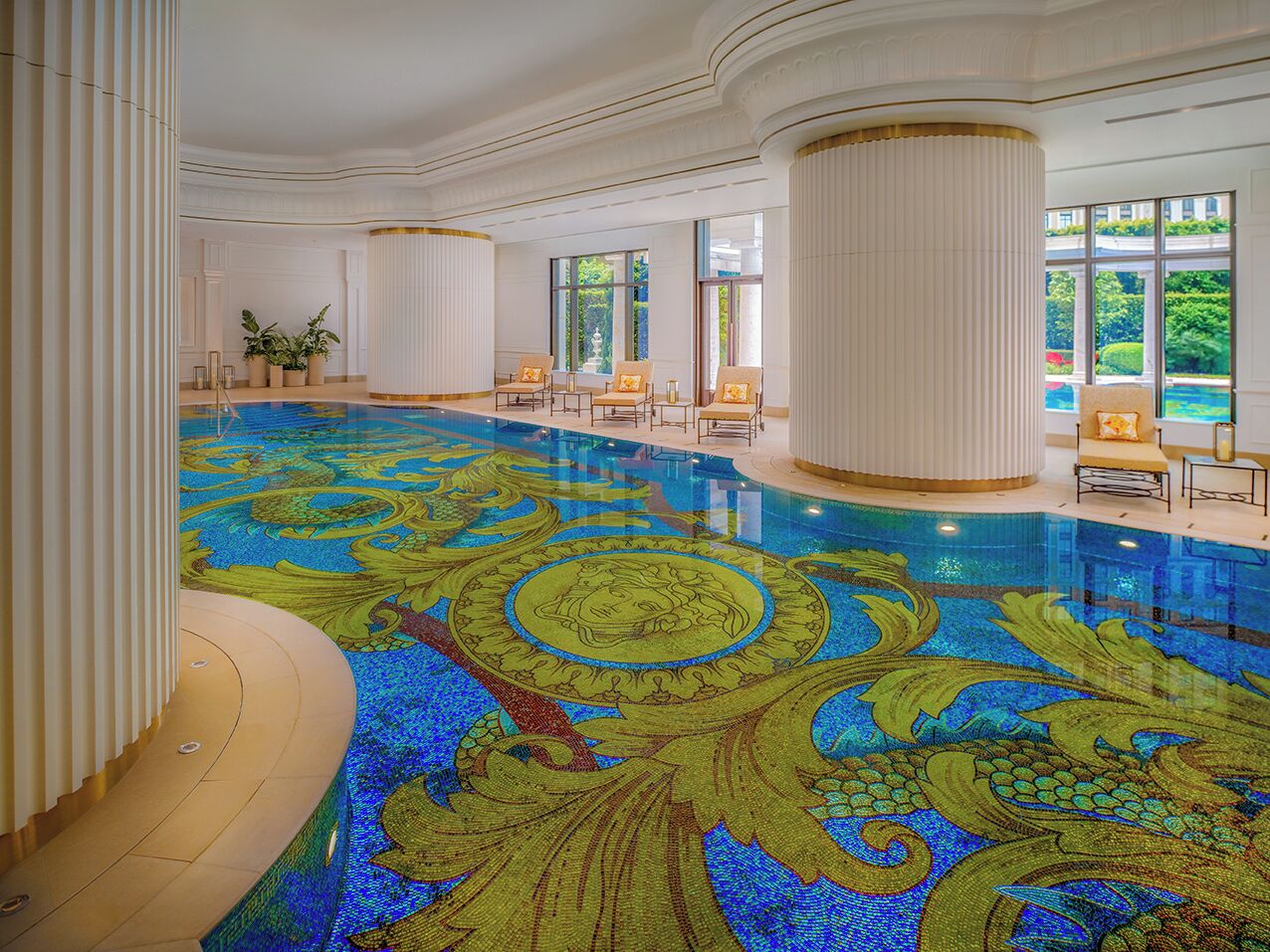 An indoor swimming pool with a decorative floor, columns, and seating areas.