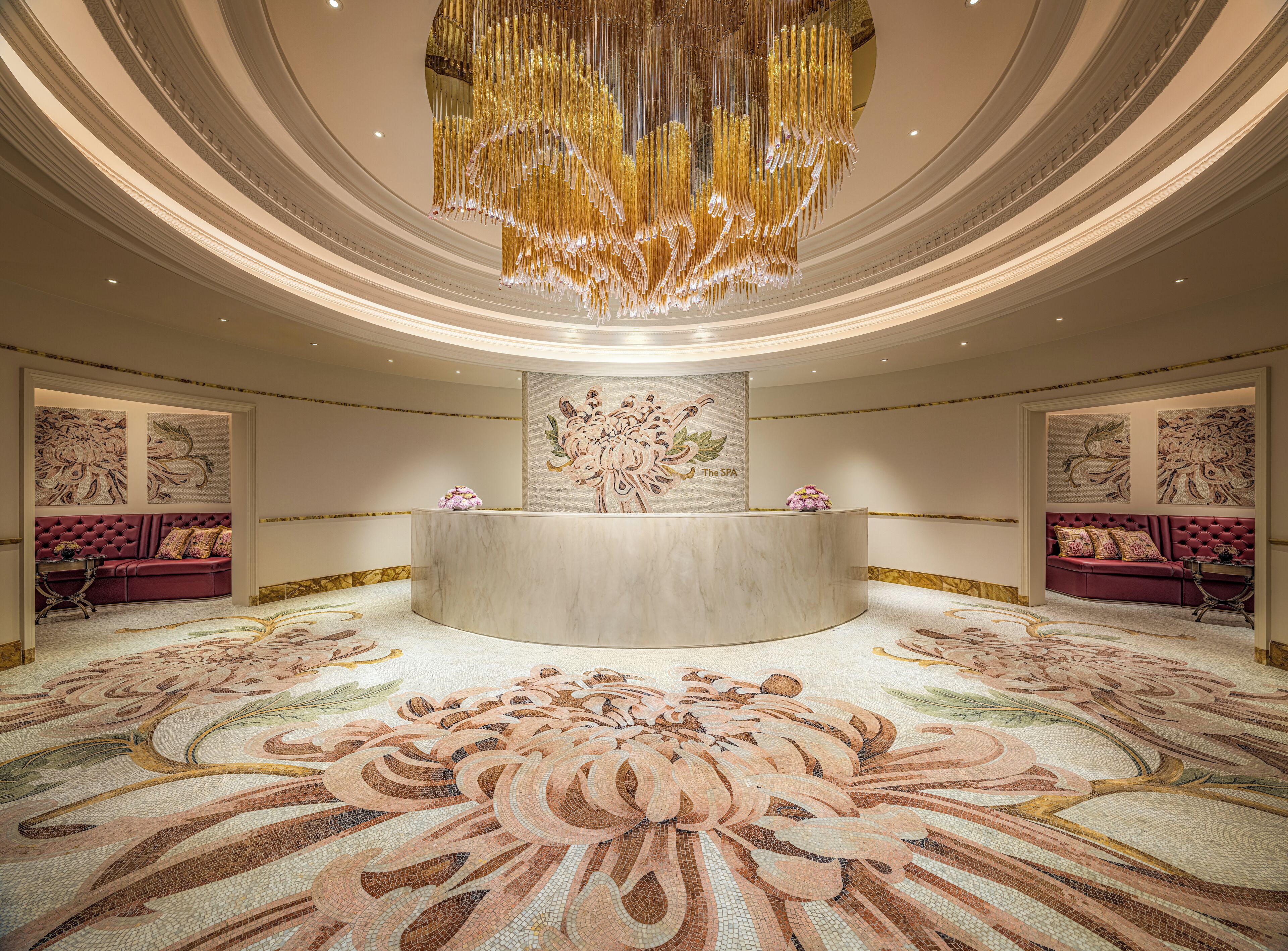 Un lobby lujoso con un mostrador de recepción de mármol, detalles de arte floral en la pared y un suelo con mosaicos elaborados.
