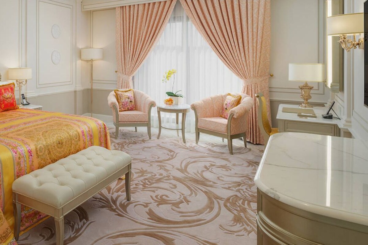 A luxurious bedroom with a large bed, a bench, two armchairs, a small table, and a vanity.