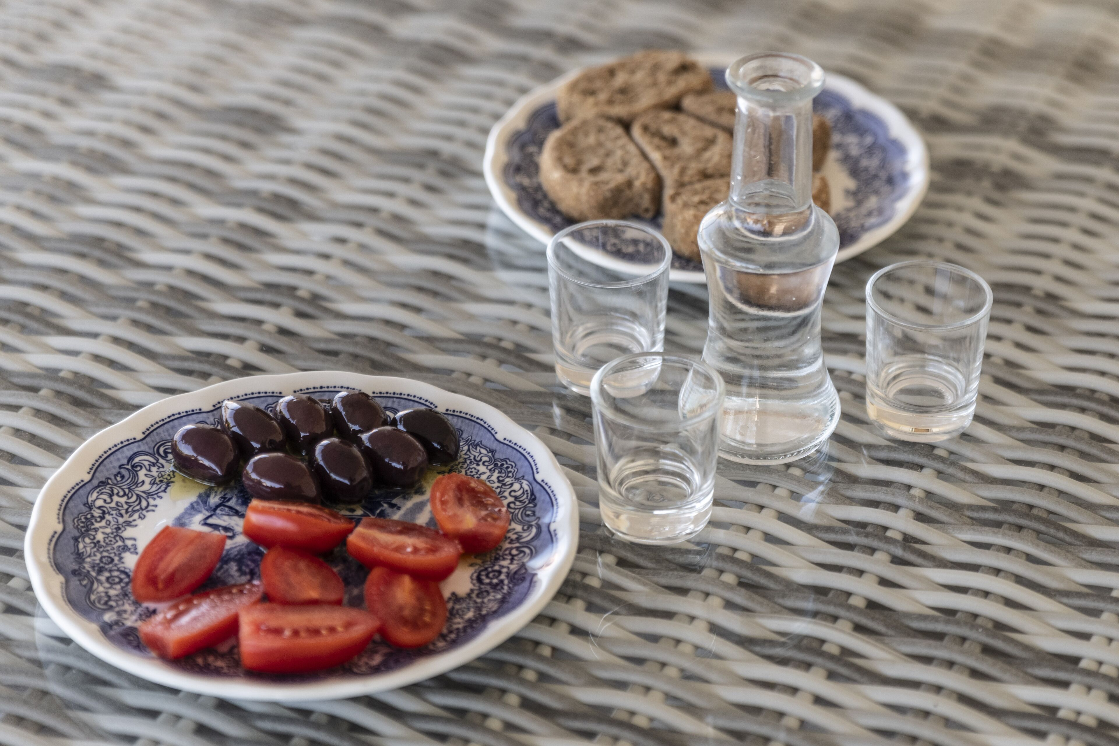 A table with two plates of food, one with olives and tomatoes, and the other with cookies and a bottle. There are also two shot glasses on the table.