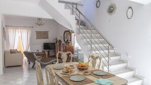 Un comedor con una mesa dispuesta para cuatro personas, una escalera y una sala de estar al fondo.