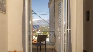 Una puerta corrediza de vidrio abierta que da a un balcón con una silla y una mesita.