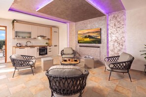 A modern living room with wicker furniture, a kitchen in the background, and a large landscape painting on the wall. - Villa Vilani Spa & Pool, Krasica, Croatia (Krasica)