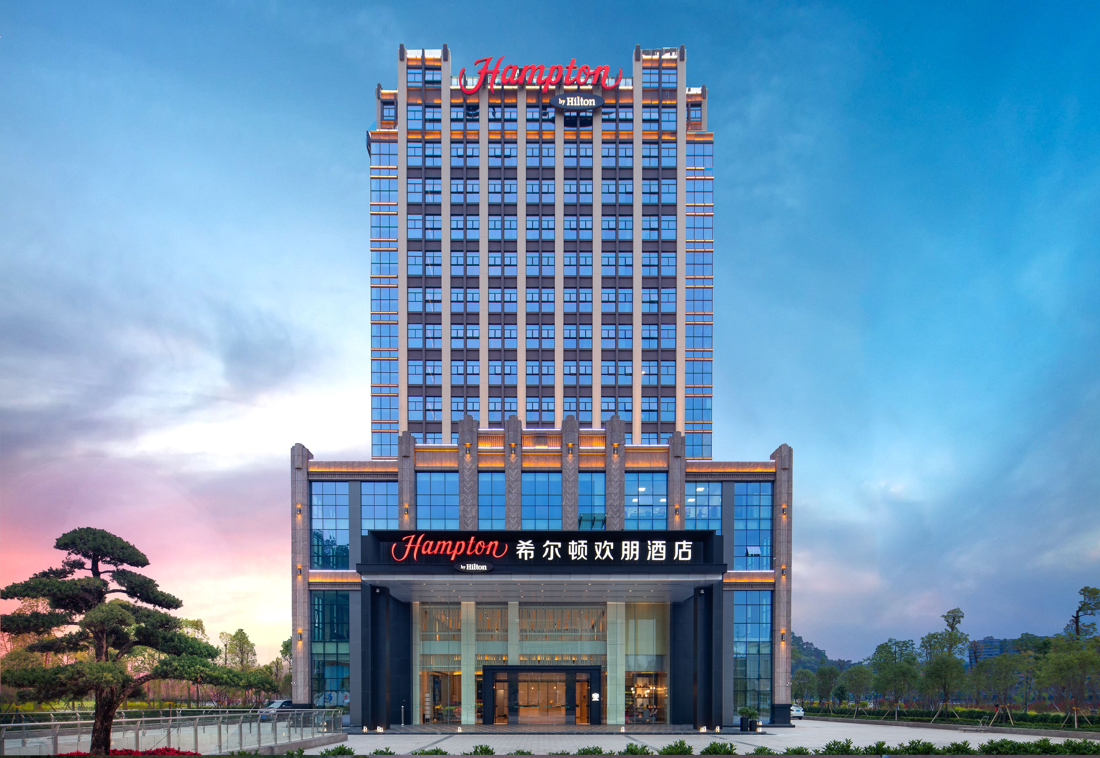A tall hotel building with a prominent sign reading "Hampton by Hilton" at the top.