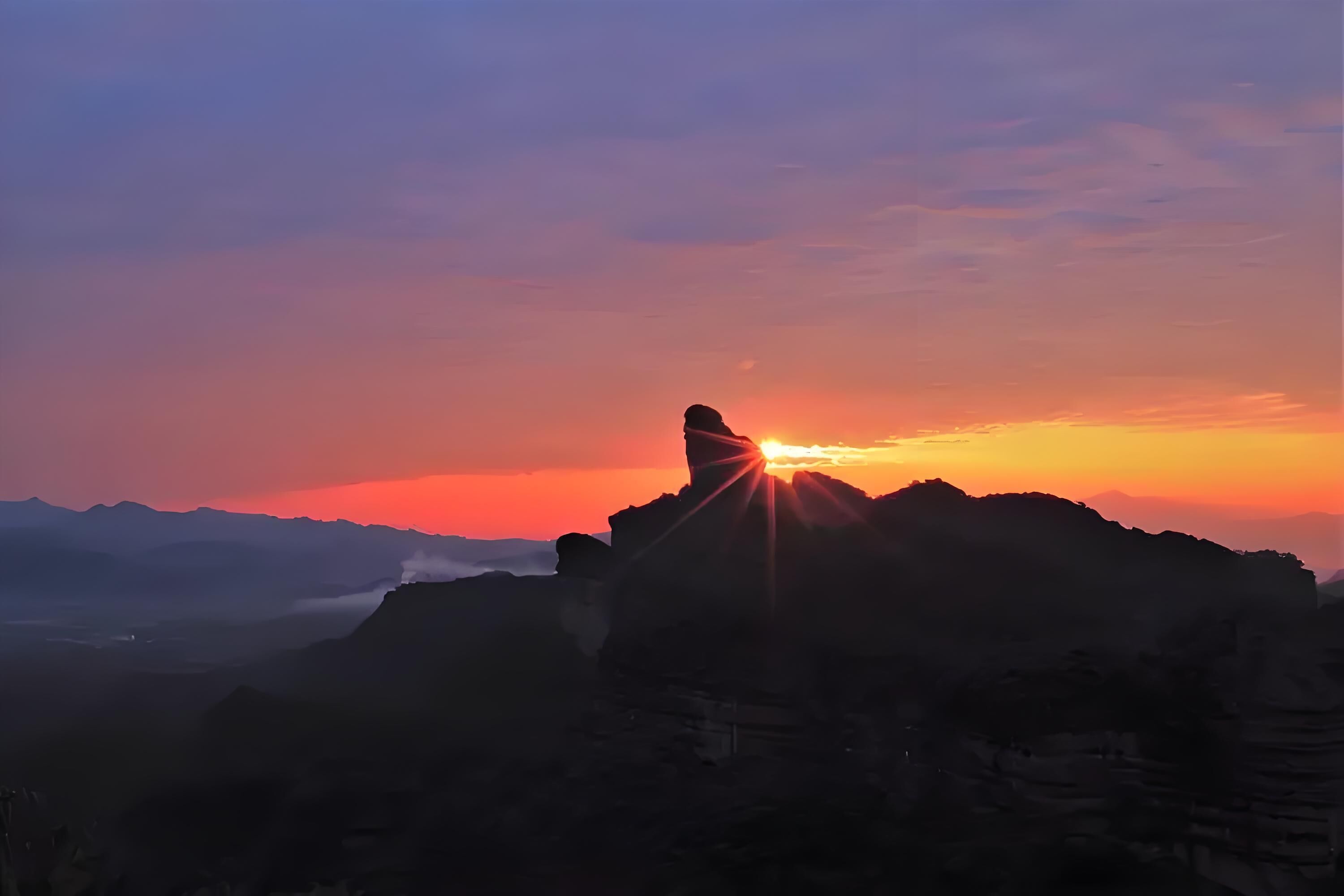 Un paysage montagneux dominé par une formation rocheuse imposante se détachant sur le ciel au coucher du soleil.