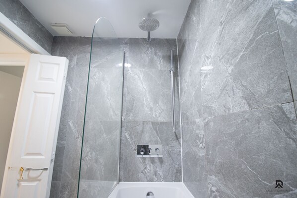 A modern bathroom with a glass-enclosed shower, marble walls, and a white bathtub. - London Apt - Sleeps 4 - Parking - Wifi (London)