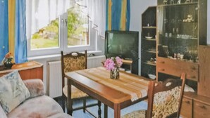 A cozy living room with a wooden table, chairs, a sofa, a television, and a cabinet with glass doors.