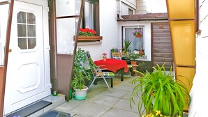 A small, enclosed outdoor area with a table and chairs, surrounded by potted plants and a door.