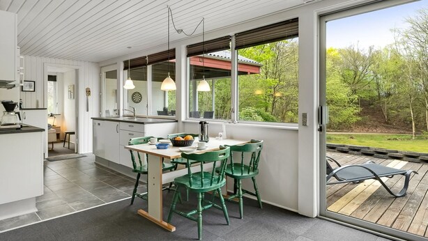Una cocina moderna con armarios blancos, un comedor con sillas verdes y un amplio ventanal con vistas al exterior.