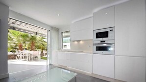 Una cocina moderna con armarios blancos, una mesa de comedor de vidrio y vistas a un patio con mobiliario exterior.