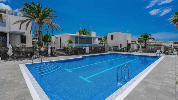 Una piscina con agua cristalina azul, rodeada de edificios modernos y palmeras.