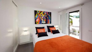 Una habitación de hotel moderna con una cama grande, un cuadro de un león colorido en la pared y un balcón con mobiliario exterior.