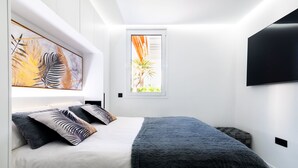 Ein modernes Schlafzimmer mit einem Bett, einem Fenster mit Blick auf Palmen und einem Wand-Fernseher.