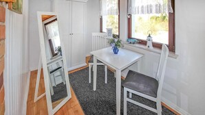 A small, white room with a table and two chairs, a mirror, a clock, and a window with lace curtains.