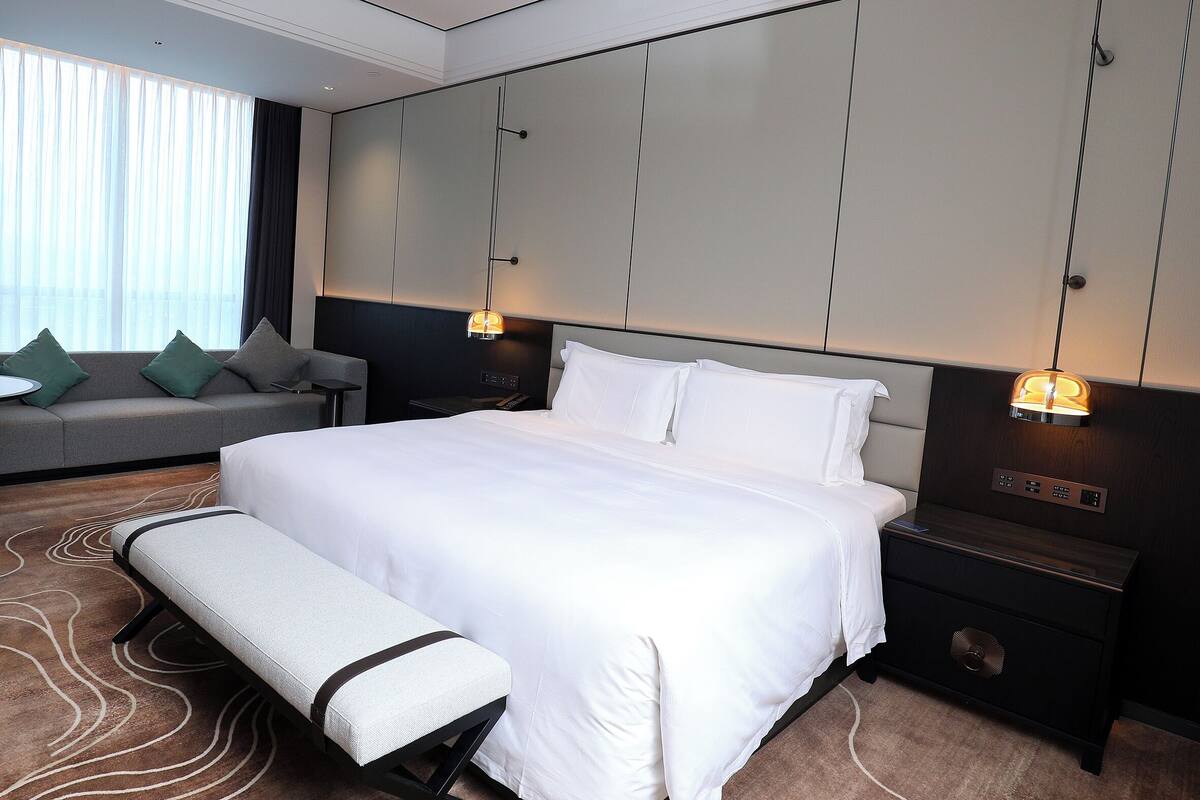 Une chambre d’hôtel moderne avec un grand lit, un canapé, une petite table et un banc.