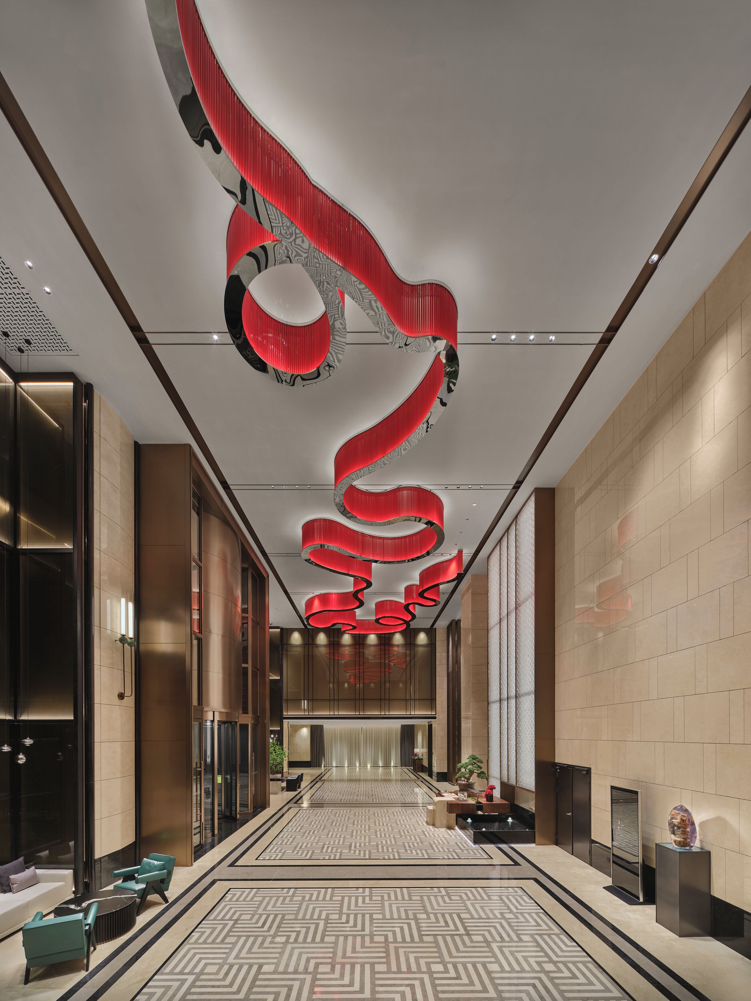 Un vestíbulo moderno con piso de diseño geométrico, un área de estar central con sofás y un diseño único de techo en espiral rojo.