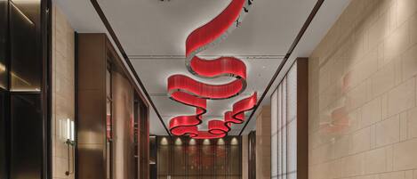 Un vestíbulo moderno con piso de diseño geométrico, un área de estar central con sofás y un diseño único de techo en espiral rojo.