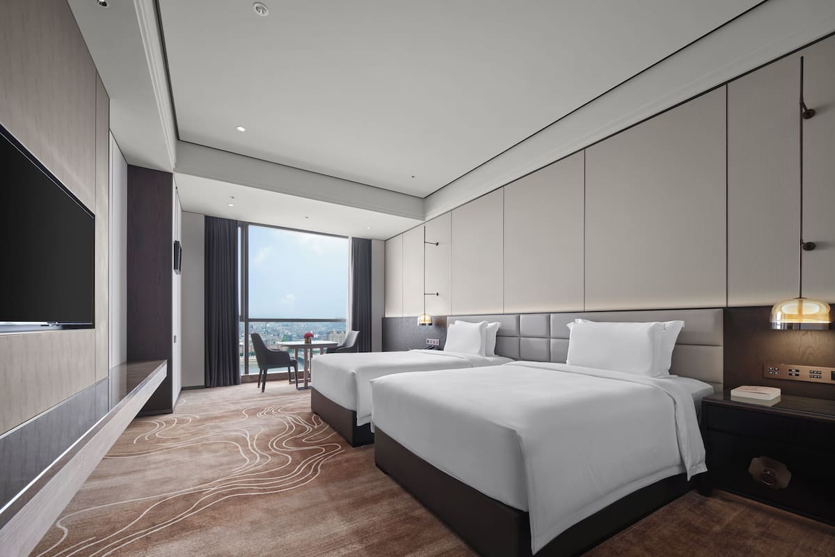 Une chambre d’hôtel moderne équipée de deux lits, d’un téléviseur à écran plat, d’un bureau avec une chaise et offrant une vue sur la ville.