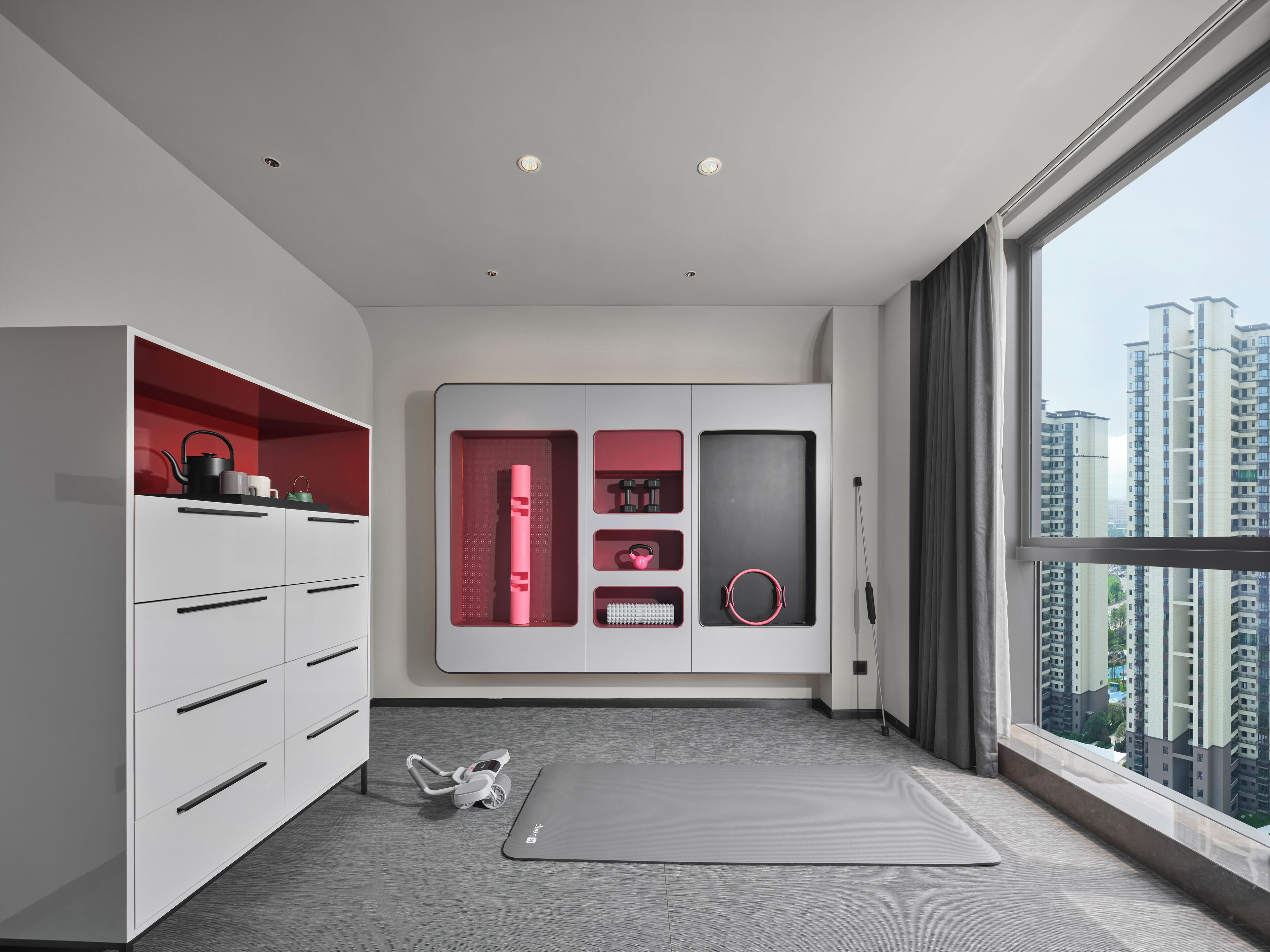 A modern apartment with a kitchen area, a workout mat, and a view of high-rise buildings.