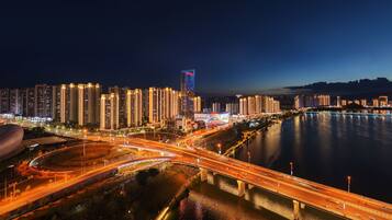 A nighttime cityscape with illuminated buildings, a river, and a bridge.