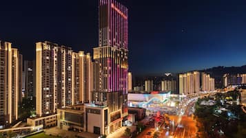 A high-rise building with illuminated signage, surrounded by other tall buildings and a busy street with vehicles.