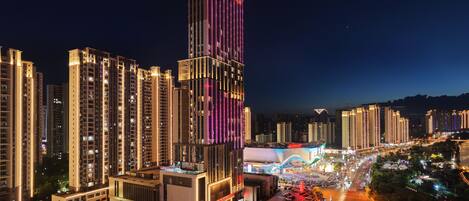 A high-rise building with illuminated signage, surrounded by other tall buildings and a busy street with vehicles.