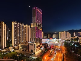 A high-rise building with illuminated signage, surrounded by other tall buildings and a busy street with vehicles.
