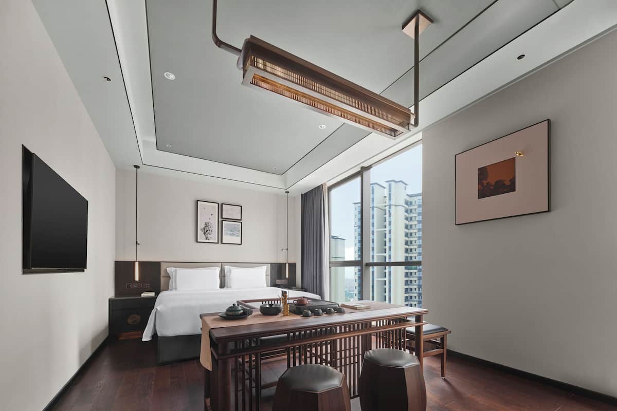 Une chambre d’hôtel moderne dotée d’un grand lit, d’un coin repas et offrant une vue sur des immeubles imposants.