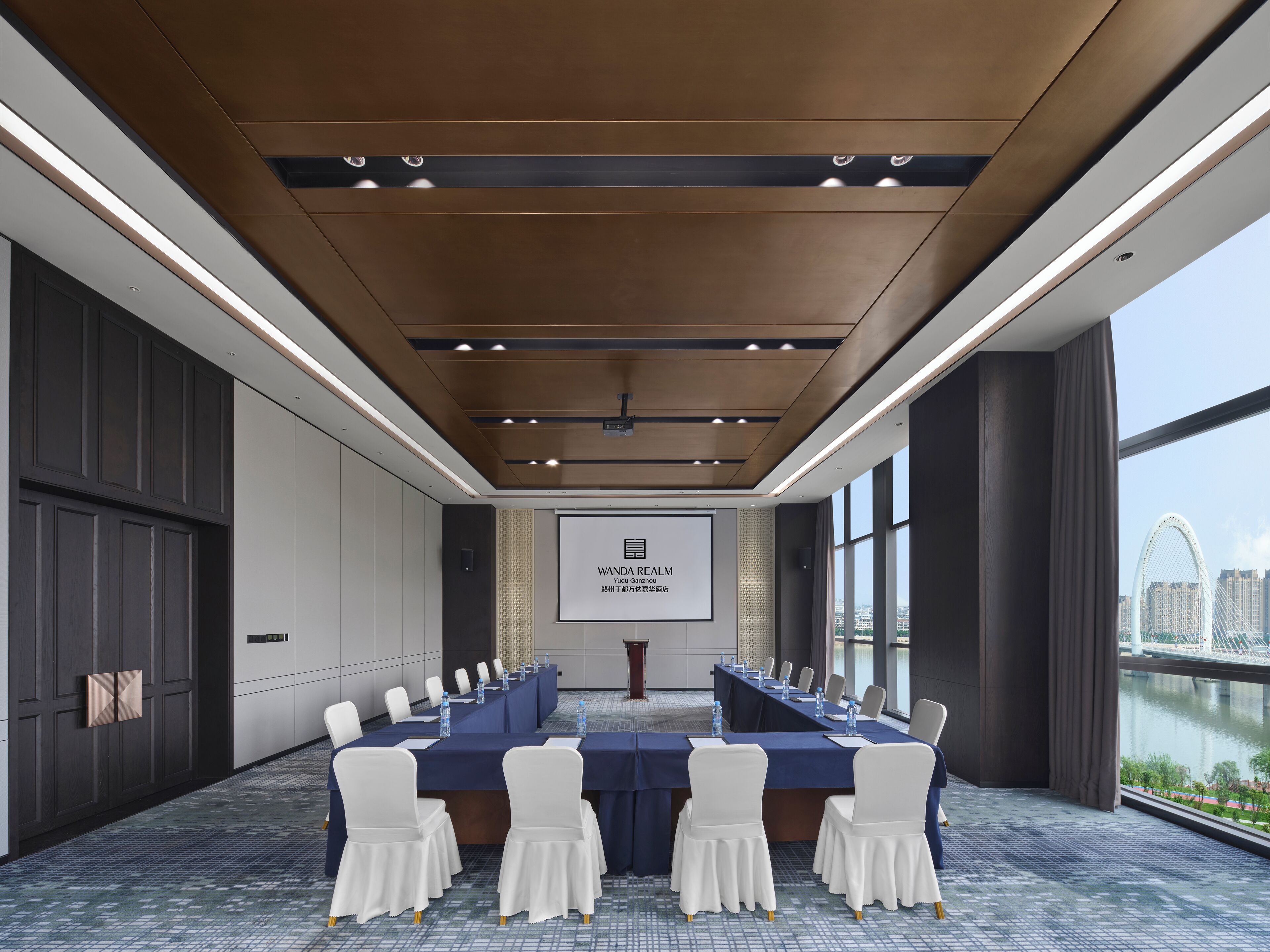 Un salón de conferencias con una larga mesa, sillas blancas y una pantalla proyectora que muestra 