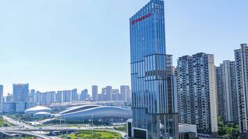 A modern high-rise building with a distinctive red logo, surrounded by other high-rise buildings and a green park area.